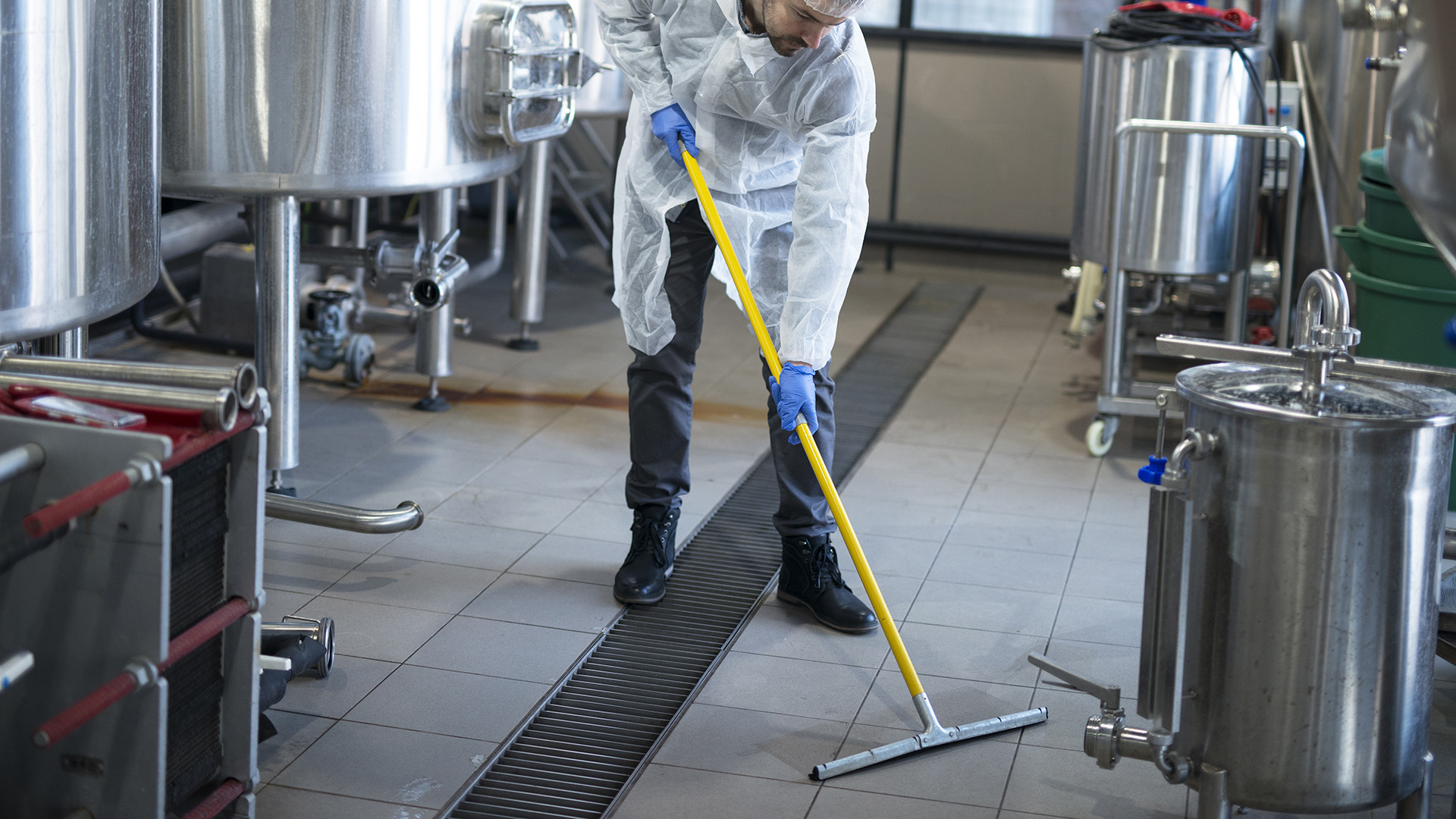 Professional cleaner wearing protection uniform cleaning floor of production plant.